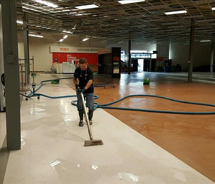 LArge warehouse with standing water on the floor. SERVPRO Employee is extracting the standing water with extractor
