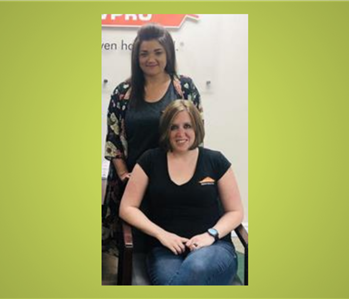 2 women in SERVPRO shirts one sitting and one standing smiling