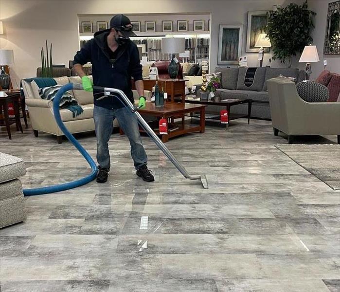 standinng water on the tile floor of a large building with a man using a water extractor tool to remove the standing water.