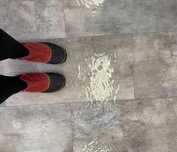 Feet wearing water boot, standing in a few inches of standing water on tile flooring